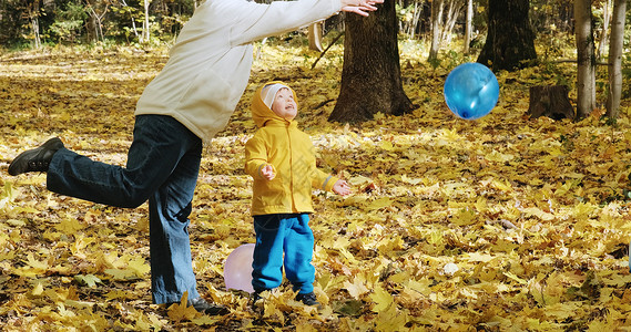 树叶中的气球小孩子和母亲玩着充气气球 秋天的大自然森林小树林家庭闲暇树叶童年乐趣数据中心叶子妈妈背景