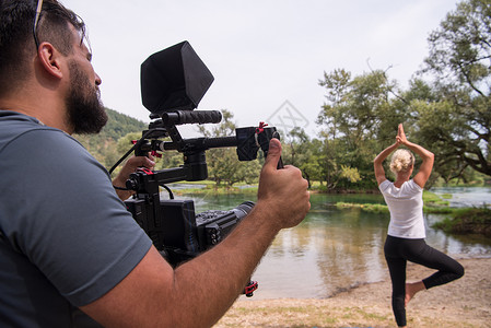 妇女做瑜伽锻炼时的年轻视频摄像员记录公园成人平衡女孩女性女士活动姿势运动摄像师背景图片