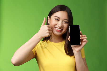 特写满足可爱的亚洲女孩给予积极反馈 竖起大拇指显示智能手机屏幕 介绍很棒的新应用程序 推荐好的应用程序 在游戏中吹牛打分企业家工背景