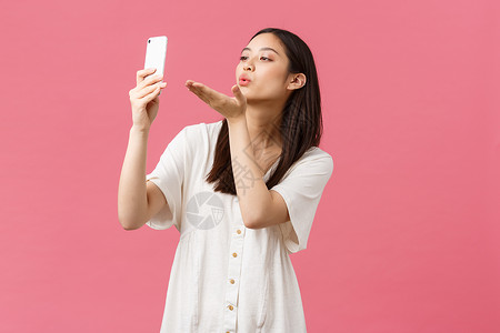 美 人的情感和技术概念 女性漂亮时尚的亚洲女博主在智能手机相机上自拍 直播在应用程序上向粉丝发送飞吻 粉红色背景背景图片