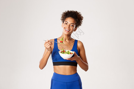 健康的生活方式和体育概念 有吸引力的年轻健身女子穿着蓝运动服装 吃沙拉和微笑 站在白色背景上 (笑声)背景图片