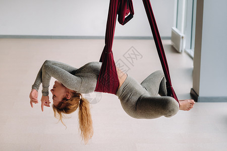灰色吊床一个女人挂在吊吊吊吊床上 在健身房做瑜伽运动员衣服有氧运动灵活性反重平衡灰色工作室女士冥想背景