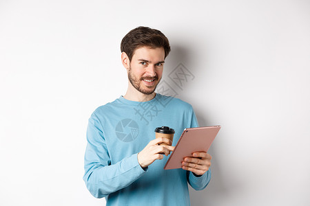 英俊的长胡子男子在镜头前微笑 喝咖啡和阅读数码平板电脑上 站在白色背景之上胡须咖啡店生活发型快乐杯子促销办公室情绪成人背景图片