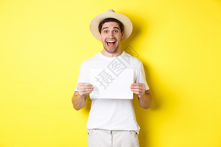 兴奋的旅游者展示你的标志或空白纸上的标牌 笑着惊讶地微笑 站在黄色背景之下促销旅行假期技术游客情绪快乐手势帽子广告背景图片