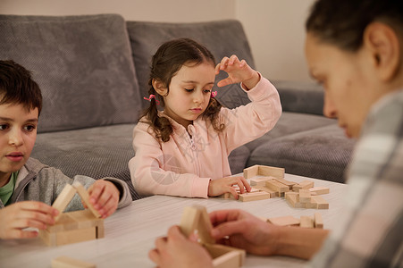 游戏力精细运动技能 专注力发展 教育休闲 家庭消遣理念 可爱的孩子和模糊的妈妈玩棋盘游戏 专注于在前景中建造木结构背景