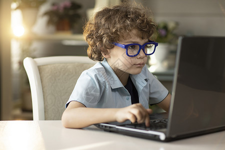 韩式卷毛男孩戴眼镜的卷毛男孩正在用笔记本电脑书 仔细看监视器屏幕小学头发键盘房间媒体男生家庭注意力智力背景
