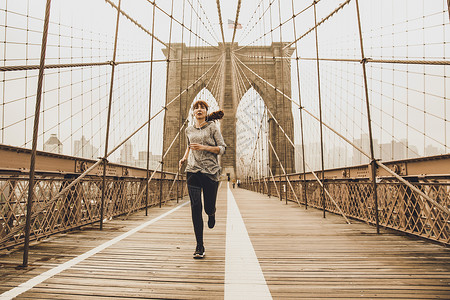 奔跑在布鲁克林桥上跑步耳机赛跑者城市慢跑者训练锻炼音乐女性运动员背景图片