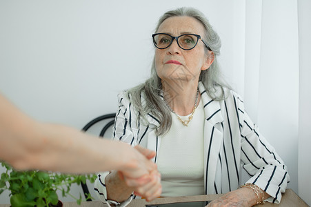 成熟的女商务人士正在领导与新同事的访谈 最后摇动手握着他们的手夹克成人员工女士眼镜老年成功经理女性退休背景图片