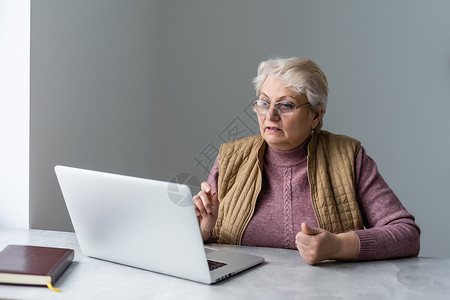在家里或办公室工作的严肃成熟的老年妇女在笔记本电脑上观看培训网络研讨会 60 多岁的中年女商务人士在使用计算机技术时做笔记用户教背景图片