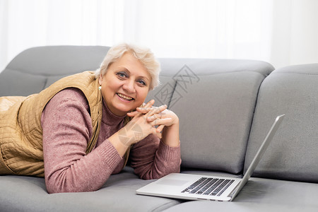 在家里或办公室工作的严肃成熟的老年妇女在笔记本电脑上观看培训网络研讨会 60 多岁的中年女商务人士在使用计算机技术时做笔记课程程背景图片