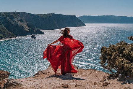 一个穿红裙子的头发松散的女孩在黄岩石上挥舞着她的裙子 俯视海面 阳光从太阳升起来到海里女性衣服热情天后女士成人衣冠发型欲望幸福背景图片