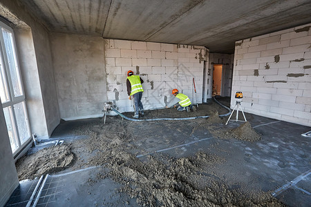 两名工人在正在建设的建筑物的公寓中使用气力输送机和测速仪 准备制作水泥地坪背景图片