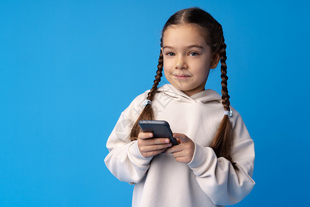 使用手机的小女孩 蓝色背景女孩与蓝底女孩相比微笑娱乐电话童年孩子们白色乐趣享受细胞技术背景图片