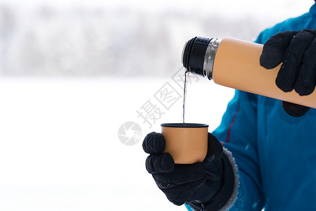 蓝色手把女性用手把热茶或咖啡倒进杯子 从冬季森林的热水池中吐出来 在寒冷的天气下喝着温暖的饮料背景