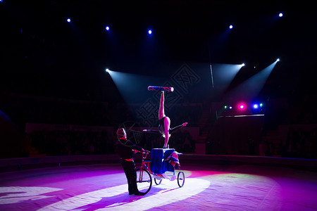 在马戏团圆顶下骑自行车的杂耍家剧院男人姿势艺术女孩体操空气空中飞人演员娱乐背景图片