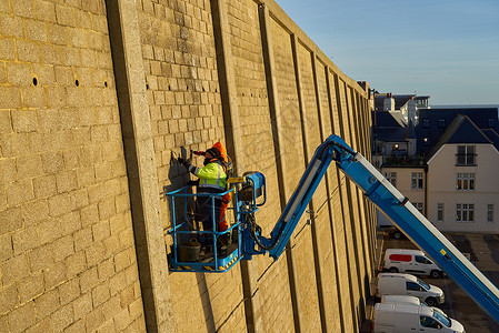 铰接式男人修复高悬崖墙 在繁荣臂上蓝色动臂天线工业手臂作业工地工程系统高度背景