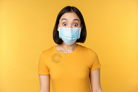 身戴医疗面罩的韩国女孩脸部肖像在黄色背景上站立 对新闻感到惊讶 惊异的反应面具互联网女士成人保健横幅卫生疫苗学生大学背景图片