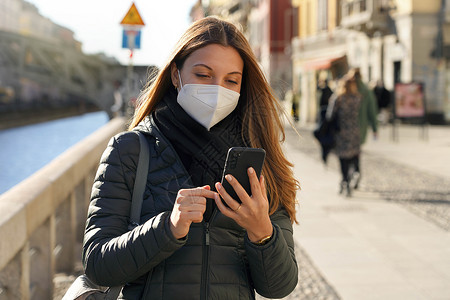 冬季在城外穿着强制性面罩保护面具使用手机行走的美丽女子 身戴强制防伪面具背景图片