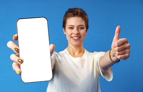 一名年轻女性在蓝背景上站立时展示空白屏幕移动电话的纵向肖像微笑广告手指营销相机成人女孩手机女士细胞背景图片