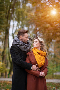 在秋天的公园里 一缕阳光照在这对恩爱的情侣身上 男人和女人从背后相拥而笑 面带微笑 一对热恋中的年轻夫妇玩得很开心的户外照片 色背景图片