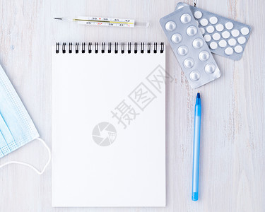 医生办公室的桌子最顶端视图 打开纸条 上面有空白页 药品 笔 面罩 温度计 写一个治疗计划背景图片