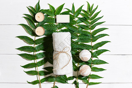 用毛巾和肥皂装在白木背景上 绿色叶子玻璃勺子花瓣浴室瓶子收藏桌子化妆品女性芳香背景图片