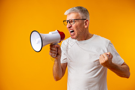 成年男子在黄色背景下用扩音器喊叫的肖像商业销售退休体积喇叭公告商务白发眼镜注意力背景图片
