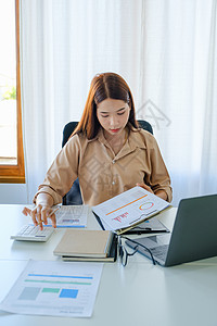 一位女性公司员工正在使用计算器通过互联网在平板电脑屏幕上计算销售收入技术数据营销货币投资经理文档人士金融桌子背景