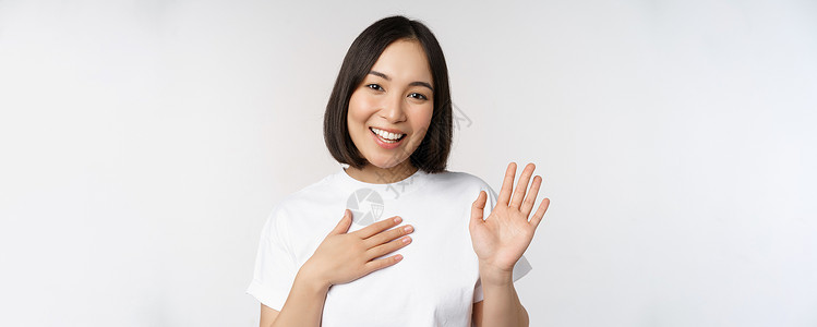 美丽的韩国女孩举手的画像 自我介绍 手放在心上 问候 站在白色背景上成人学生商业购物大学情感女性女士工作技术背景图片