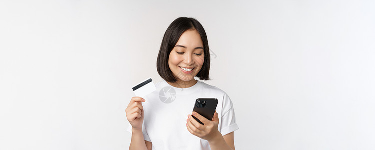 网上购物 快乐的亚洲女性使用信用卡和智能手机应用程序 通过手机在网站上付款 白色背景成人情绪女孩女士企业家银行业互联网购物女朋友背景图片