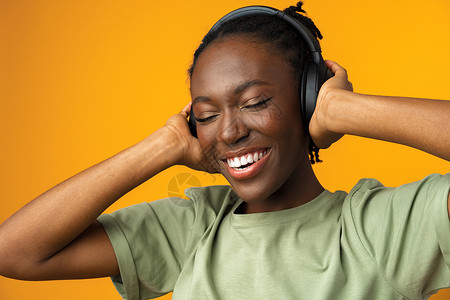 黑色黄底快乐的非洲裔美国年轻女性在黄色背景下用耳机听音乐 在黄底背景下女士歌曲工作室情绪化旋律喜悦幸福黑色水平收音机背景