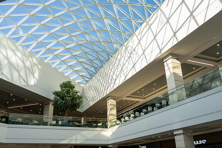 格罗特现代大型购物和娱乐综合体的内地 Trinity有一个透明的玻璃屋顶 笑声走廊蓝色金属地面反射购物中心店铺建筑学民众社论背景