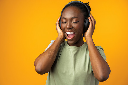 黑色线控耳机快乐的非洲裔美国年轻女性在黄色背景下用耳机听音乐 在黄底背景下水平喜悦爆炸黑色播放歌曲旋律幸福享受收音机背景