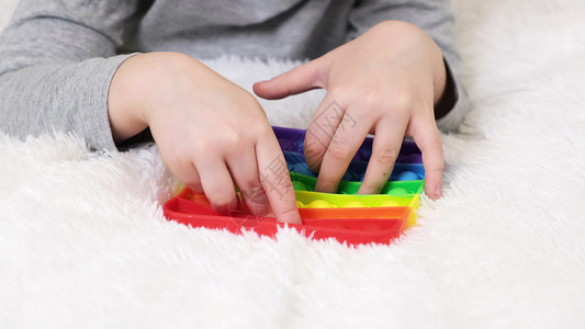 小男孩的手正在玩教育游戏 五颜六色的抗压力感官玩具坐立不安推它在幼儿的手中 抗压流行流行玩具 彩虹感官坐立不安 新潮硅胶玩具背景
