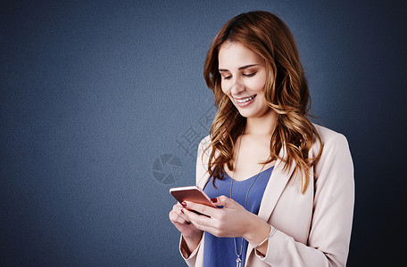 与客户沟通的最快方式 一个有吸引力的年轻女商务人士在深蓝色背景下使用手机的工作室拍摄背景图片