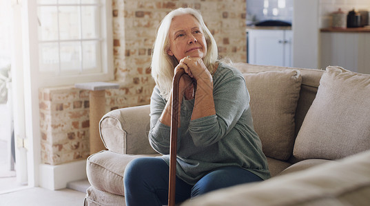我想静静我想知道我今天能做什么 照片中一位老年妇女独自坐在家里的沙发上 手里拿着手杖 看上去若有所思背景