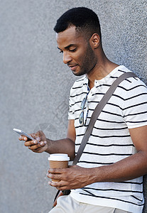 一位英俊的非裔美国商务人士 在使用他的手机时 靠着城墙靠着一面墙站着背景图片