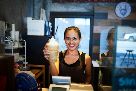 柜直冷一位年轻的咖啡师的肖像 在咖啡店里举着一杯冷咖啡喝的饮料背景