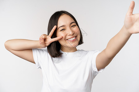 位高权重字牌美丽的亚洲年轻女性自拍 用和平 V 字牌摆姿势 开心地笑着 拍照 在白色背景下摆姿势女朋友情感女士技术大学购物工作横幅广告成人背景