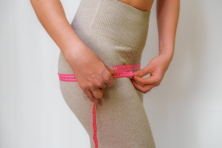 在家里用卷尺测量臀部的苗条女人的剪影 特写 一位面目全非的欧洲女性在室内检查减肥饮食或抽脂的结果 健康的生活方式磁带尺寸腹部营养背景图片