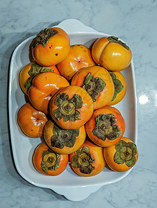 厨房桌上的新鲜每西蒙红色水果卡基宏观盘子生产食物橙子异国橙色背景图片