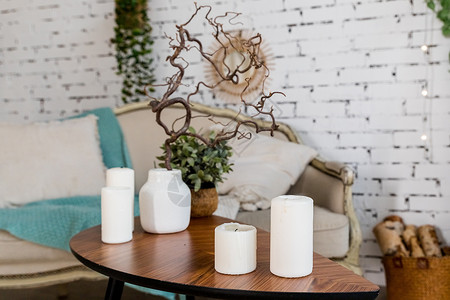 舒适客厅内部木制咖啡桌上的白色蜡烛 时尚的斯堪的纳维亚客厅 斯堪的纳维亚设计沙发前小木桌上的花瓶中的蜡烛和植物 波西米亚风家居室背景图片
