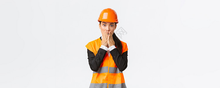 口部操担心和担忧的亚洲女性工程师在建筑区有问题 喘气和遮盖口部震惊 盯着摄影机惊慌地发出惊吓的表情 佩戴安全头盔幸福雇主维修反光经纪人背景