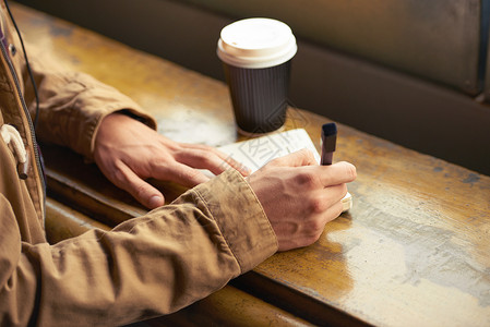 我写了一封信给我的爱人 一个男人坐在咖啡馆里在笔记本上写字的特写镜头背景图片