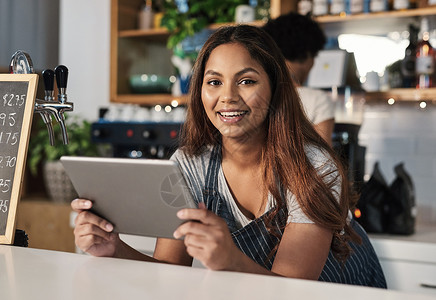店铺代运营技术是餐厅运营不可或缺的一部分 在咖啡馆工作时使用数字平板电脑的年轻女子的画像背景