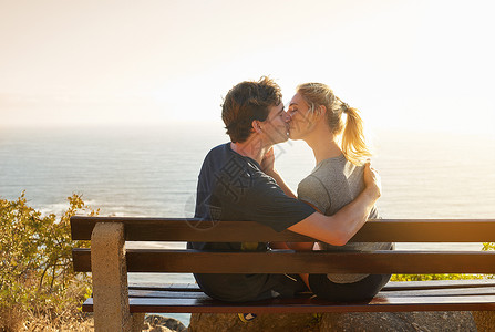 那个吻比景色美丽多了 被一对情侣坐在长椅上俯视大海的照片拍到背景图片