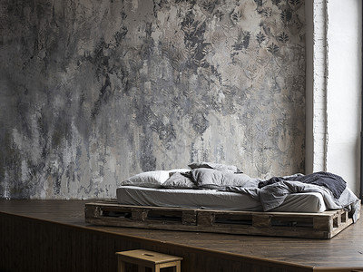 未填满的床铺 由木制板块制成 在卧室中用米盖被褥子对着有威尼斯史图科人的墙壁 斯堪的纳维亚风格背景
