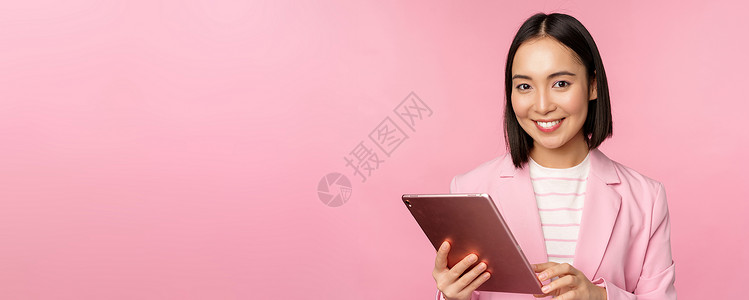 年轻亚洲公司女性的肖像 身着数字平板电脑 穿西装 微笑和看起来专业 以粉红背景作姿势的办公室女职员广告黑发商业女孩经理成人学生药背景图片