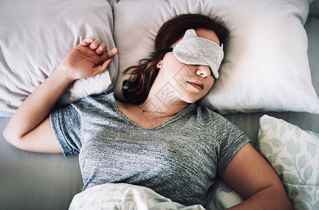 我该睡个安稳觉 一个迷人的年轻女人 在家卧室里脸上戴面罩睡觉时被拍到的高角度镜头背景图片