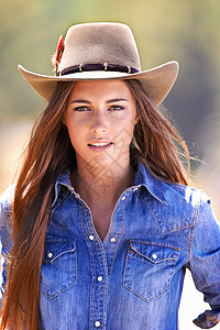 牧童野生的心 一个有魅力的年轻女牛仔站在马厩里背景